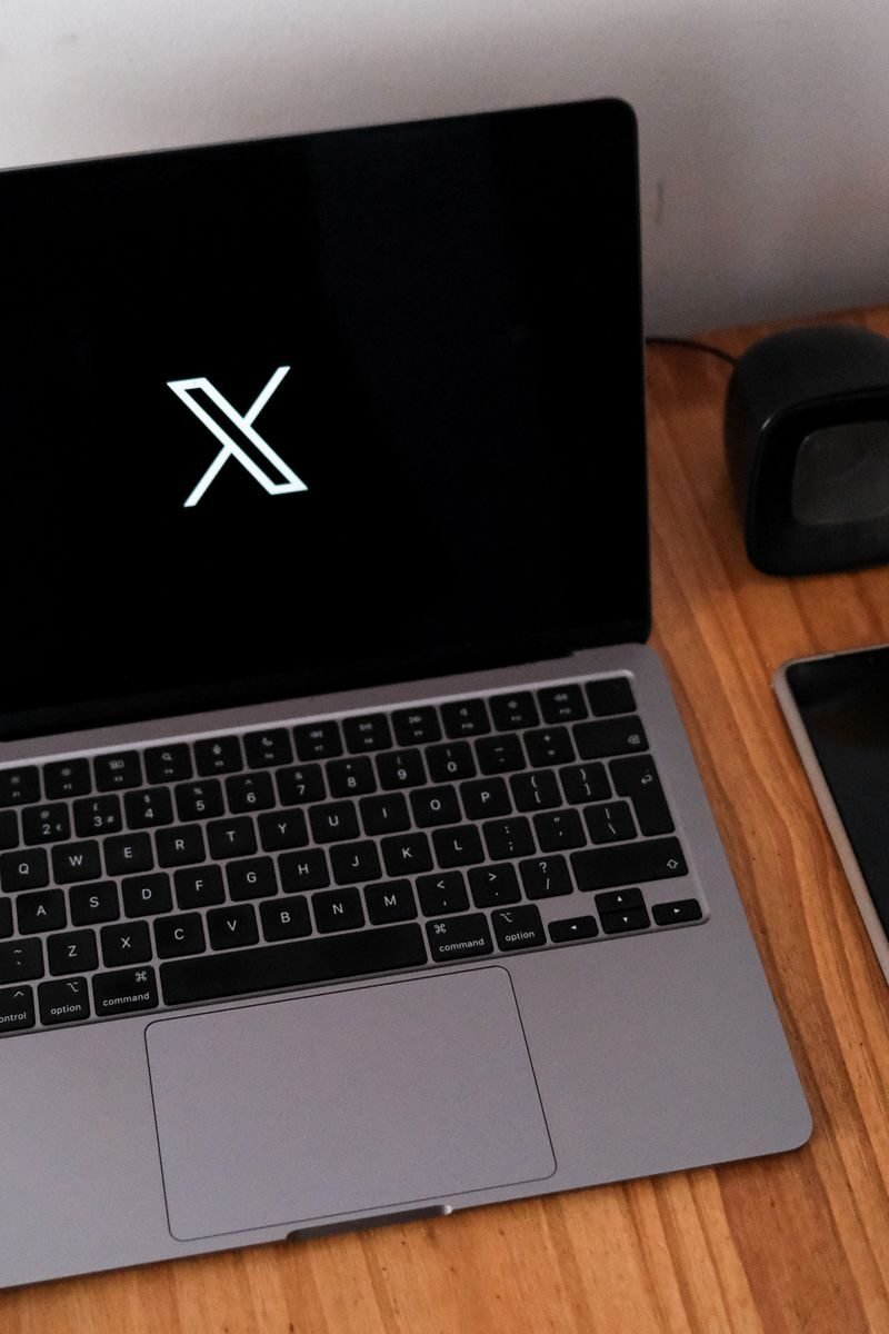 Minimalist desk setup featuring a laptop, smartphone, and clock on a wooden surface.